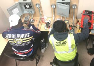 Two men working on electrical equipment in a room.