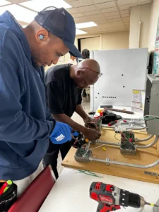 Two people working on electrical systems inside a house